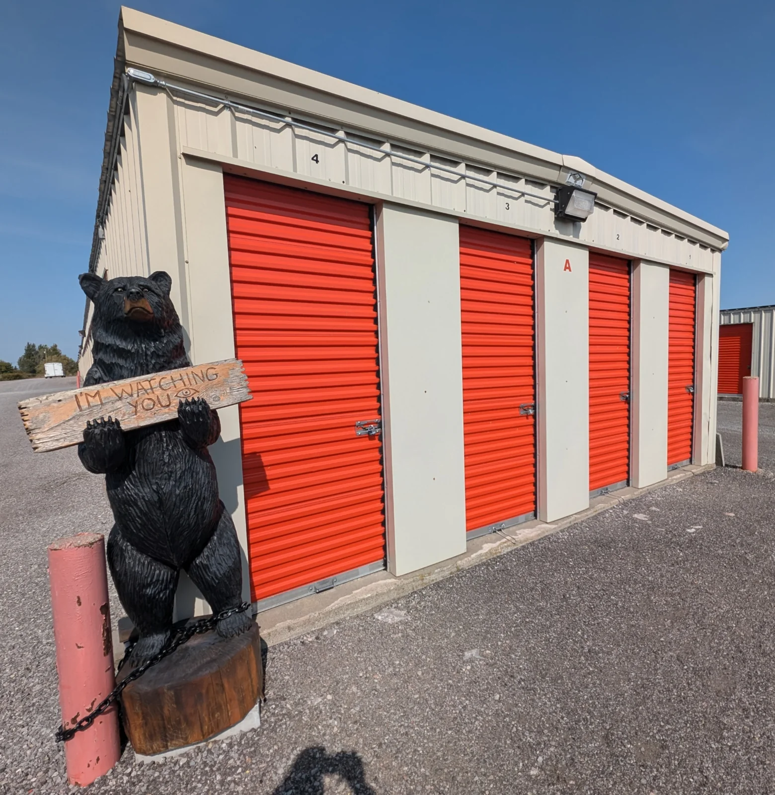 Bear statue holding an I’m watching you sign beside orange storage units